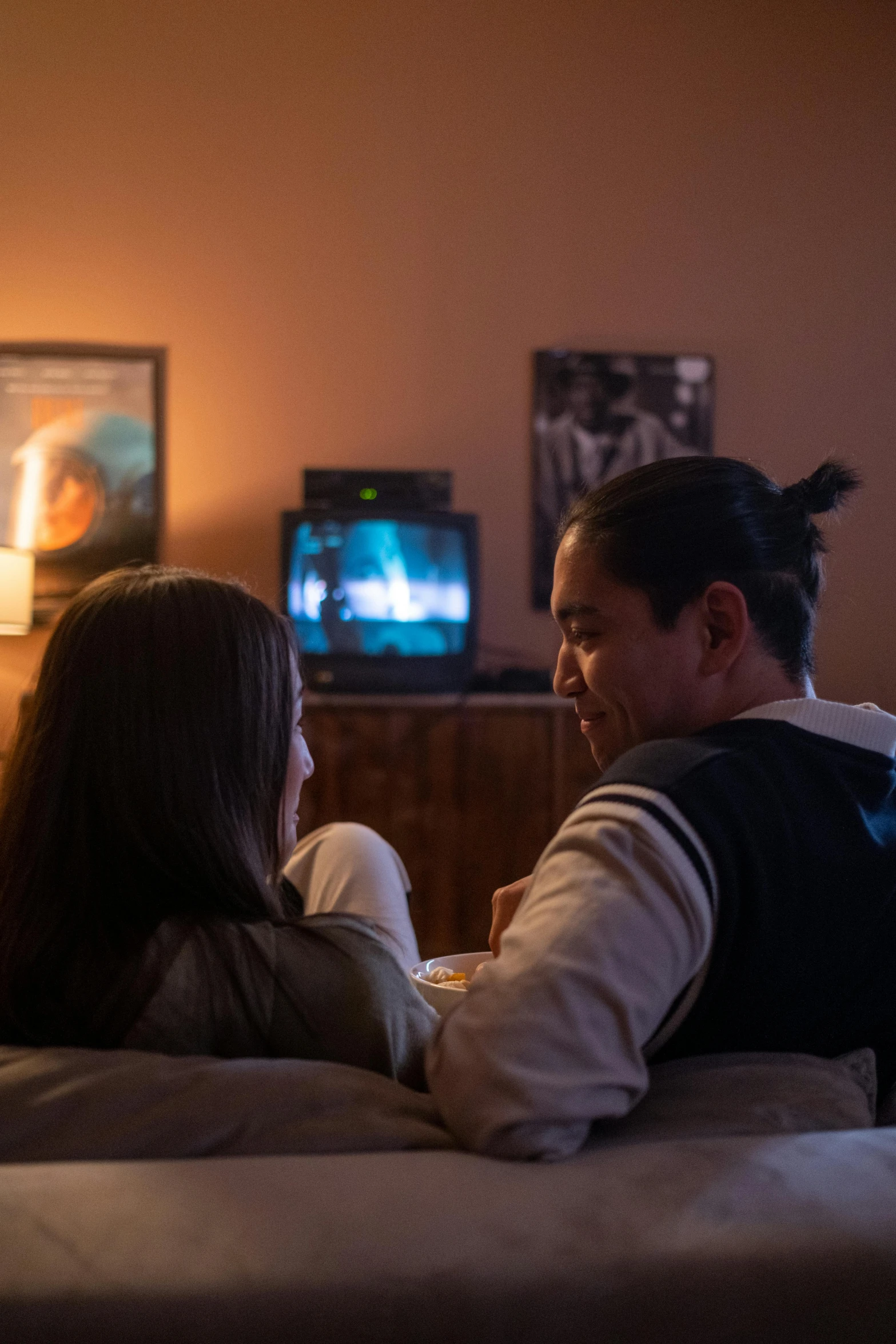 a man and a woman sitting on a couch watching tv, inspired by Nan Goldin, happening, still from alita, asian man, warm glow, back - shot