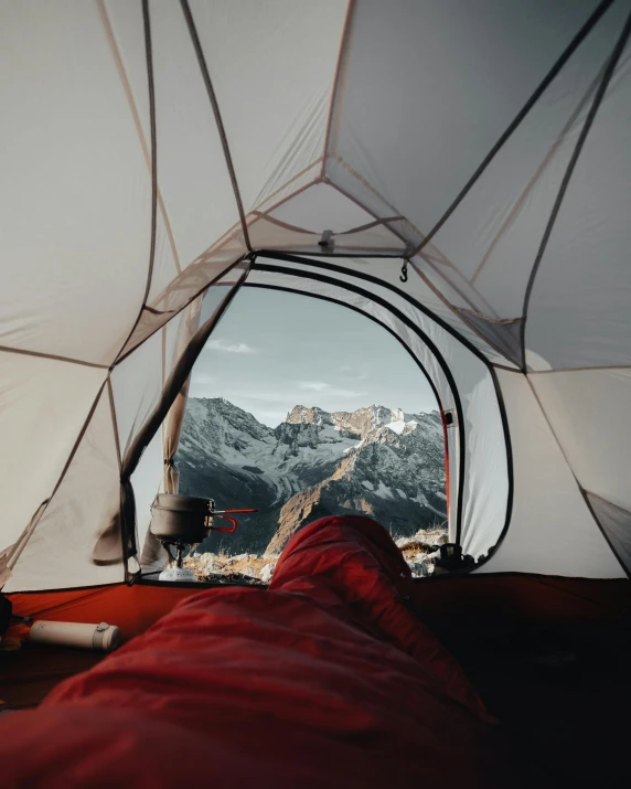 a person laying inside of a tent with mountains in the background, by Sebastian Spreng, unsplash contest winner, red brown and white color scheme, bed on the right, space seen outside from a window, high - angle view