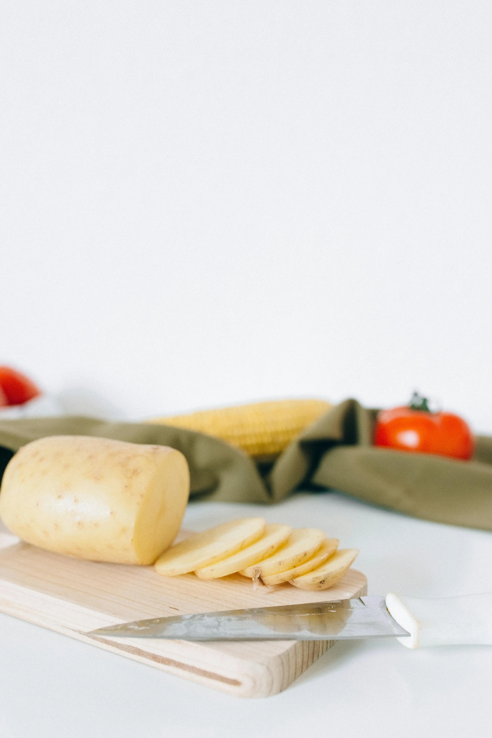 a piece of cheese sitting on top of a cutting board, pexels contest winner, potatoes, on a white table, background image, corn