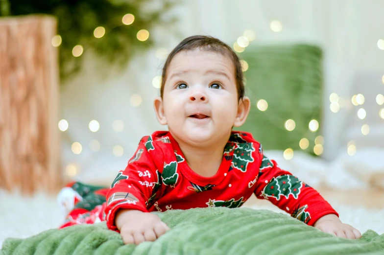 a baby laying on top of a green blanket, pexels contest winner, hurufiyya, wearing festive clothing, avatar image, christmas lights, closeup - view