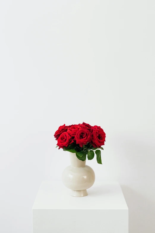 a white table topped with a vase filled with red flowers, a marble sculpture, by Luma Rouge, unsplash, rumble roses, plain background, group of seven, tufted softly