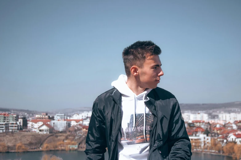 a man standing in front of a body of water, prague in the background, streetwear, background image, male teenager