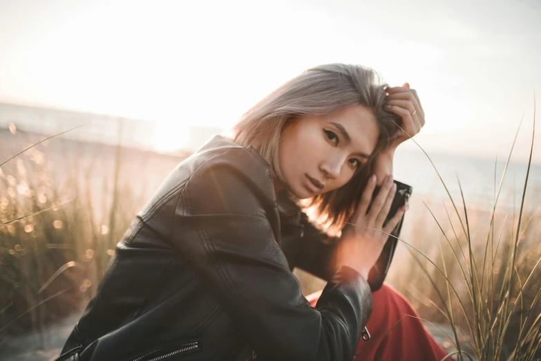 a woman sitting on top of a sandy beach, trending on pexels, realism, she wears leather jacket, girl silver hair, beautiful young asian woman, sitting in a field