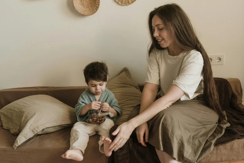 a woman sitting on top of a couch next to a child, pexels contest winner, ready to eat, beige, brown, small