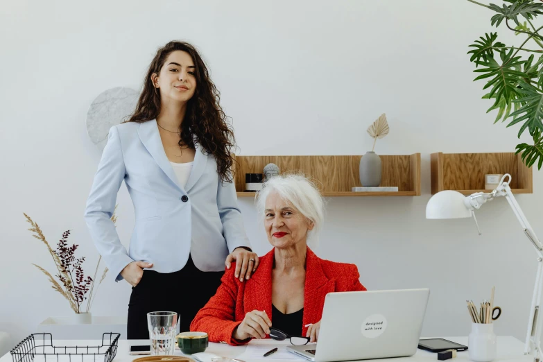 a woman standing next to a woman sitting at a desk, by Matija Jama, pexels contest winner, white haired lady, white backround, hip corporate, various posed