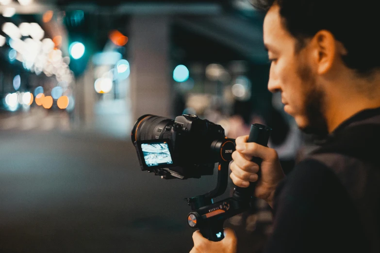 a man holding a camera on a city street, unsplash, night time footage, graded with davinci resolve, instagram picture, headshot