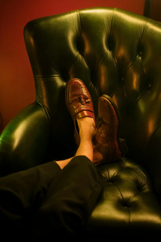 a person sitting in a chair with their feet up, inspired by Nan Goldin, renaissance, dapper, in a pub, black loafers, in the gryffindor common room