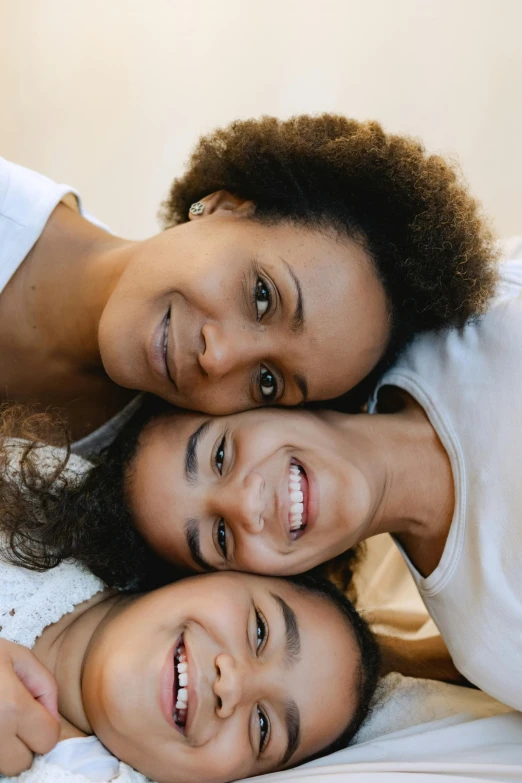 a couple of women laying on top of a bed, by Matija Jama, pexels contest winner, incoherents, portrait of family of three, mixed race woman, high angle closeup portrait, smiling young woman