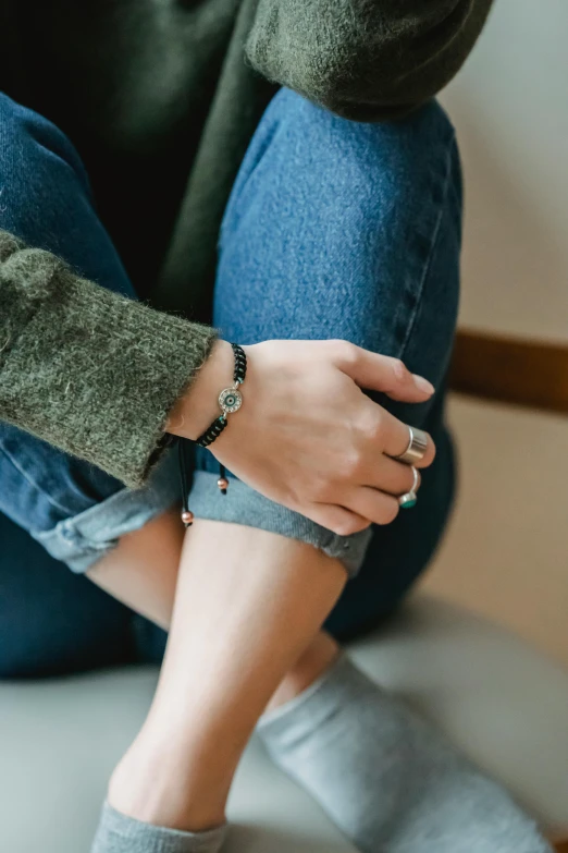 a woman sitting on the floor with her feet crossed, trending on pexels, renaissance, bracelets, wearing a jeans jackets, shungite bangle, wearing a green sweater