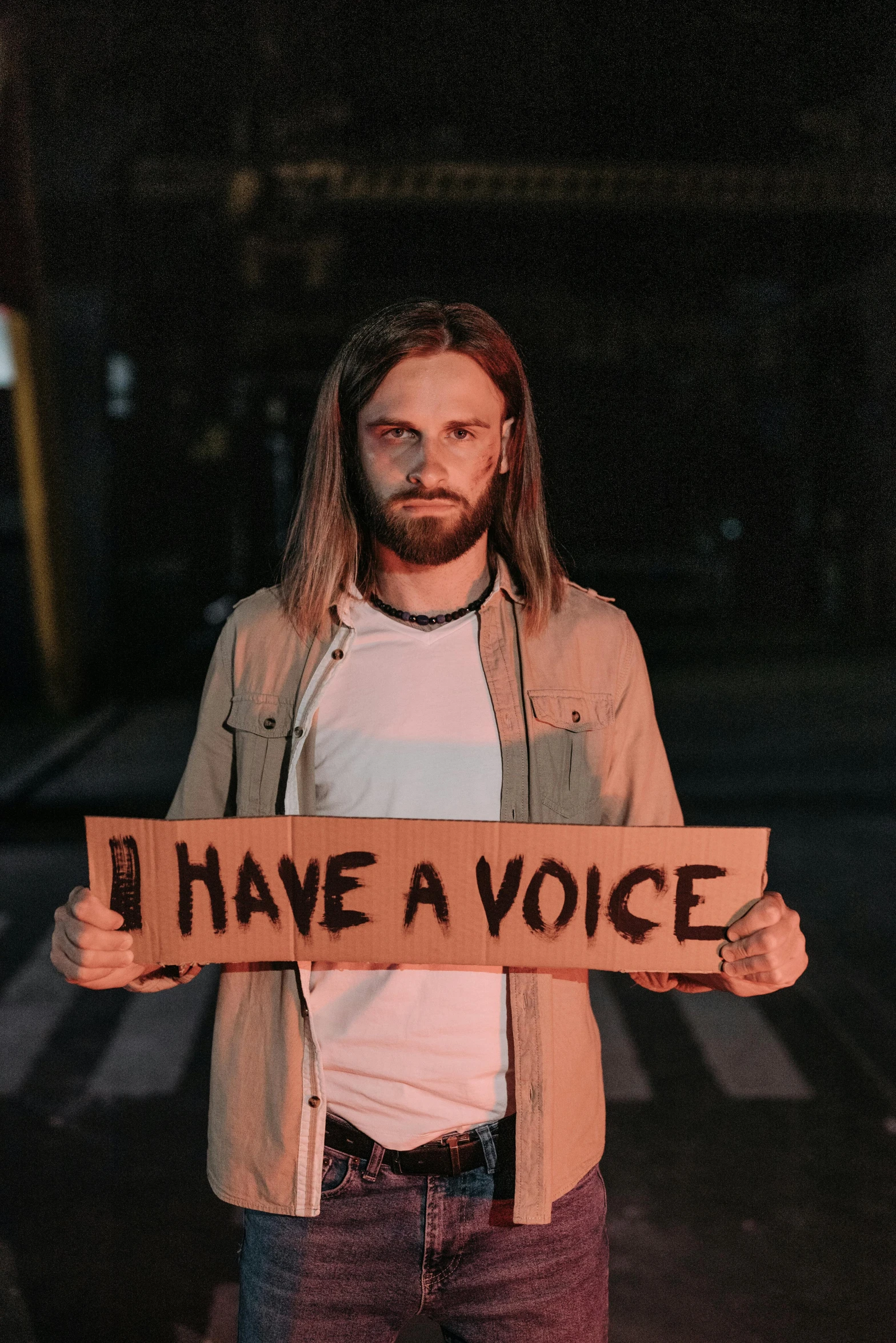 a man holding a sign that says i have a voice, an album cover, by Niko Henrichon, trending on pexels, light beard, transgender, ( ( mads berg ) ), hunger