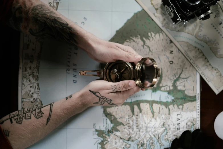 a person holding a camera on top of a map, a tattoo, pexels contest winner, orrery, holding flask in hand, thumbnail, maritime