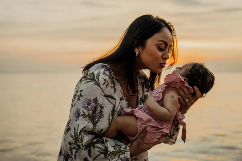 a woman holding a baby near a body of water, pink golden hour, profile image, asian women, an olive skinned