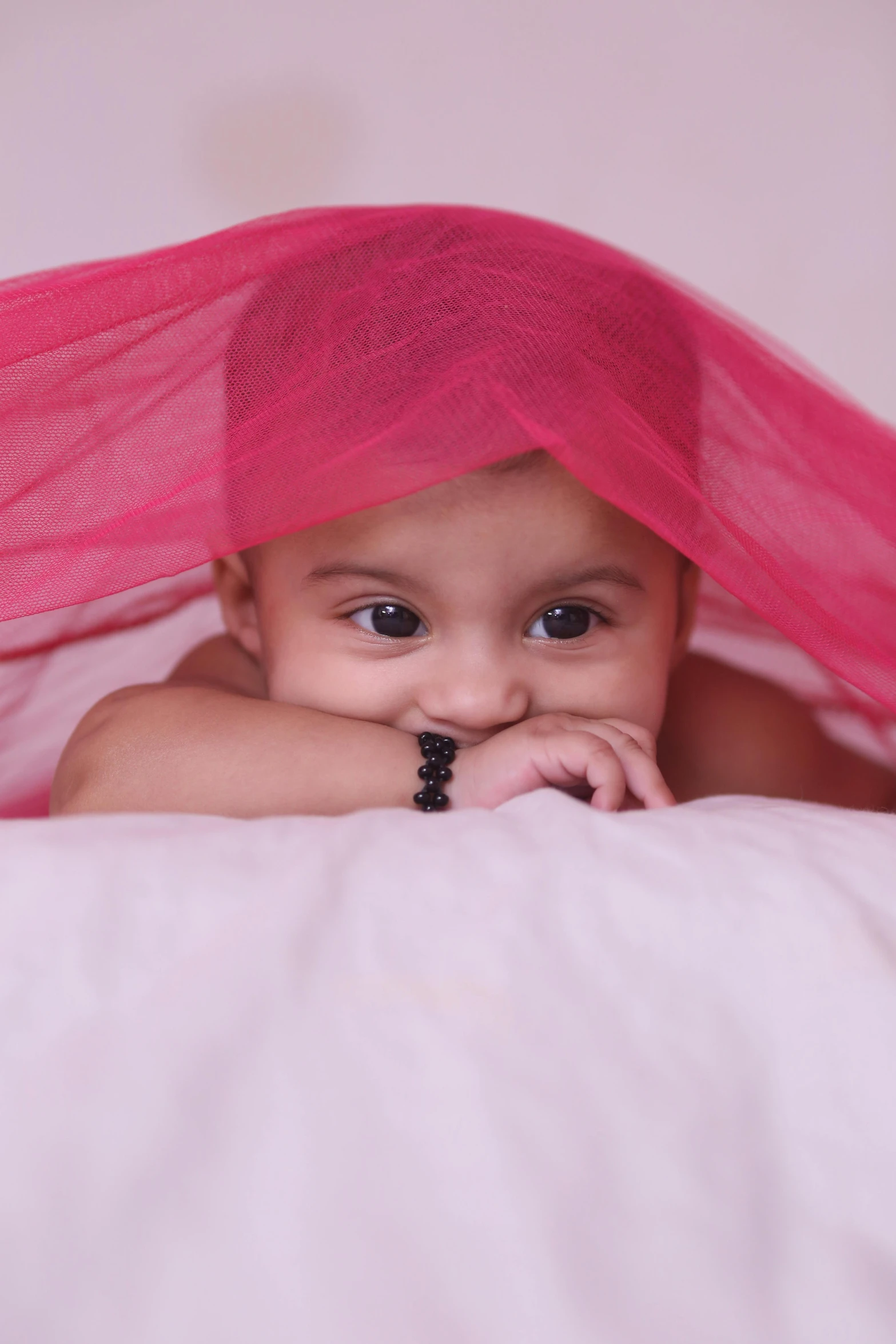 a baby laying on top of a bed under a pink sheet, shutterstock contest winner, art photography, turban, pink and black, indian, looking menacing