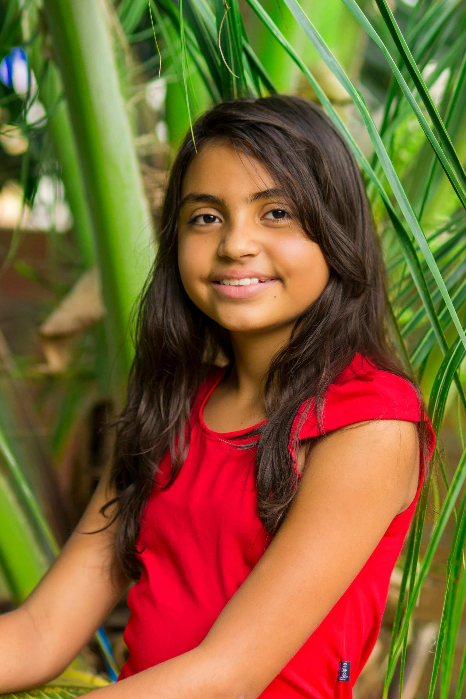 a young girl sitting on top of a palm tree, by reyna rochin, long hair and red shirt, headshot profile picture, jayison devadas, years old