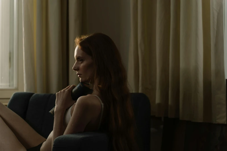 a woman sitting on a couch in front of a window, inspired by Nan Goldin, pexels contest winner, photorealism, redhead woman, dramatic lowkey studio lighting, sitting in front of a microphone, cinematic lut