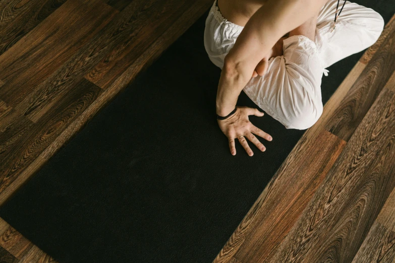 a woman doing a yoga pose on a black mat, pexels contest winner, hardwood floors, background image, hands not visible, white sleeves