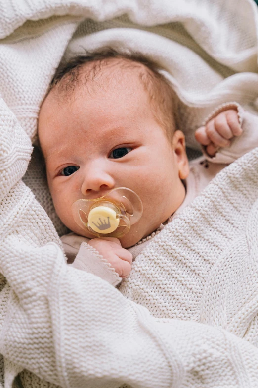 a baby wrapped in a blanket with a pacifier, a picture, by Nina Hamnett, shutterstock contest winner, gold, instagram post, manuka, medium close up portrait