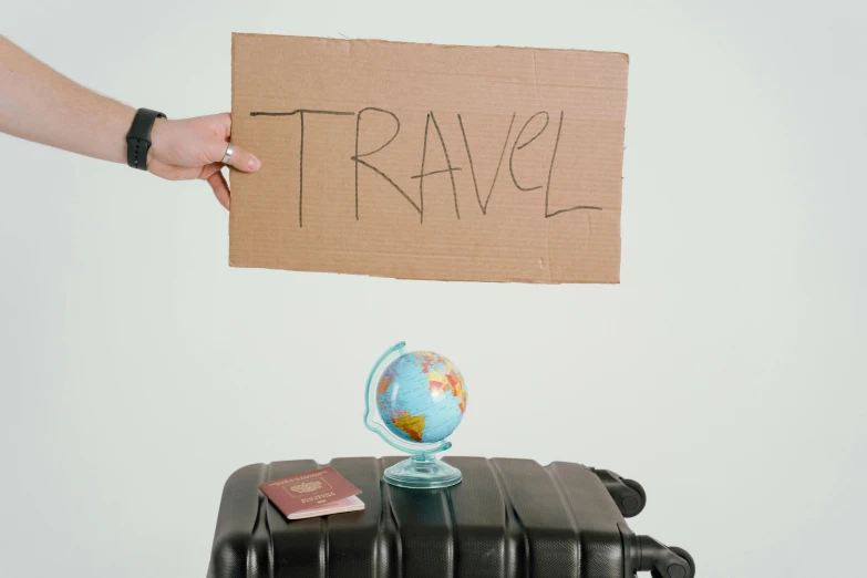 a person holding a sign above a suitcase, pexels contest winner, traverse, large globe, cut out of cardboard, jen atkin