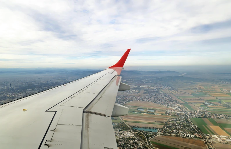 the wing of an airplane flying over a city, by Daren Bader, pexels contest winner, figuration libre, red roofs, plain uniform sky at the back, hd footage, runway