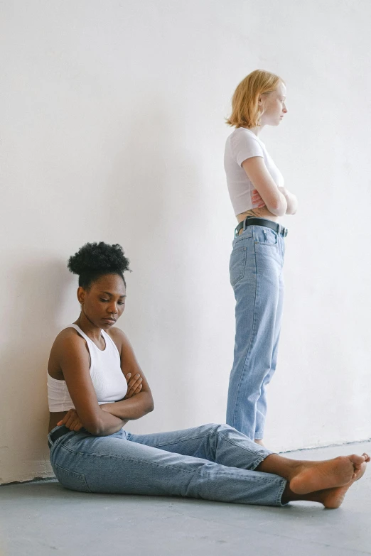 a woman sitting on the floor next to another woman, by Nina Hamnett, trending on pexels, renaissance, standing posture, depressed, varying ethnicities, wearing jeans