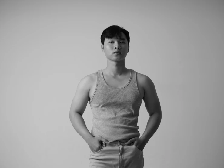 a man standing with his hands in his pockets, a black and white photo, inspired by Russell Dongjun Lu, wearing tank top, in white room, portait photo profile picture, androgynous person