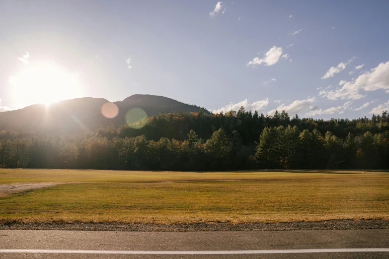 a man riding a skateboard on top of a grass covered field, unsplash contest winner, new hampshire mountain, sun shines down on the car, road between tall trees, panoramic shot