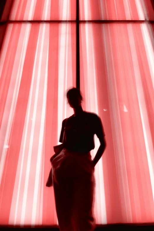 a woman standing in front of a large window, inspired by Anna Füssli, light and space, detailed red lighting, light shaft, against a red curtain, seen from below
