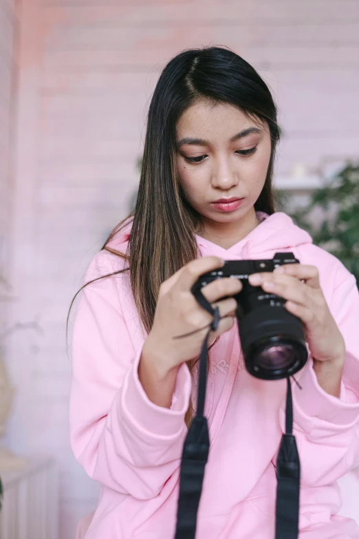 a woman taking a picture with a camera, wearing a pastel pink hoodie, cindy avelino, ps, indoor picture