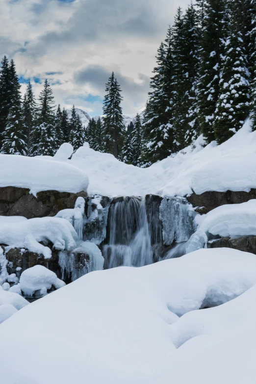 a small waterfall in the middle of a snowy forest, crater lake, slide show, whistler, distant photo