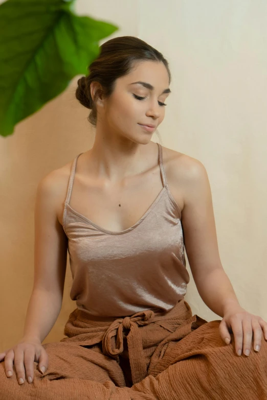 a woman sitting in a lotus position with her eyes closed, a picture, by Robbie Trevino, wearing a camisole, clay, wearing : tanktop, diffused natural skin glow