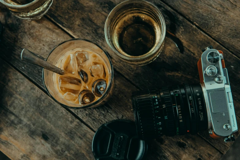 a camera sitting on top of a wooden table, inspired by Elsa Bleda, trending on pexels, whiskey glass with ice cubes, aussie baristas, medium format, iced latte