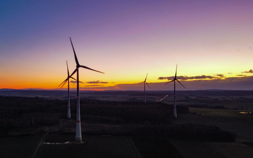 a group of wind turbines sitting on top of a lush green field, by Jesper Knudsen, pexels contest winner, sunset panorama, aerial footage, purple energy, cinematic shot ar 9:16 -n 6 -g