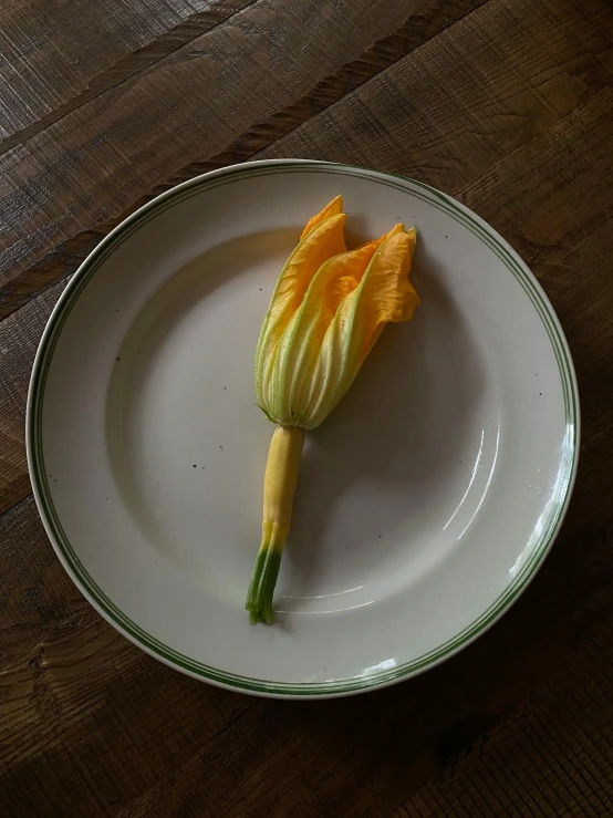 a white plate topped with a flower on top of a wooden table, inspired by Gustave Caillebotte, renaissance, gourds, lily, yellow orange, perfect shape