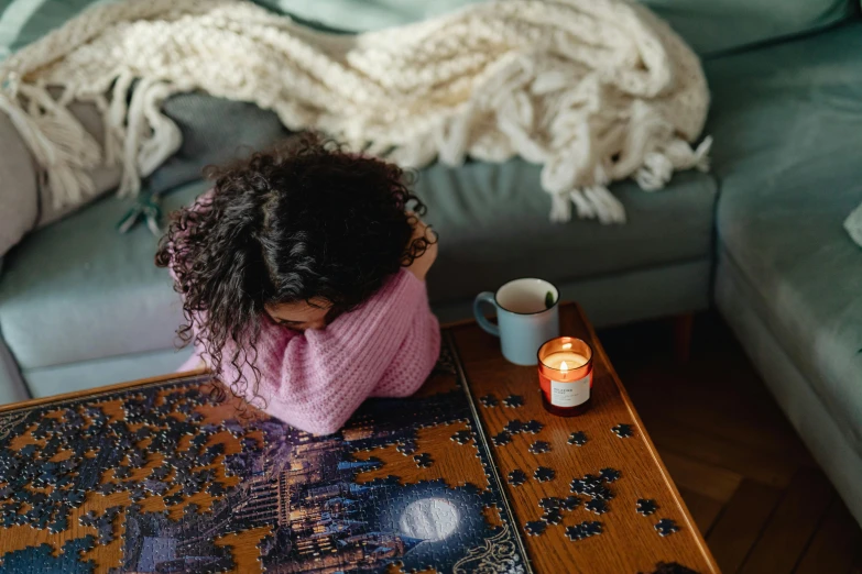 a little girl sitting on top of a wooden table, a jigsaw puzzle, by Julia Pishtar, pexels contest winner, cozy candlelight, woman very tired, sitting in a lounge, facing away