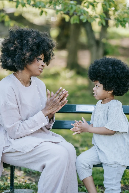 a woman and a child are sitting on a bench, by Lily Delissa Joseph, pexels, with afro, arguing, meditation, sleek hands