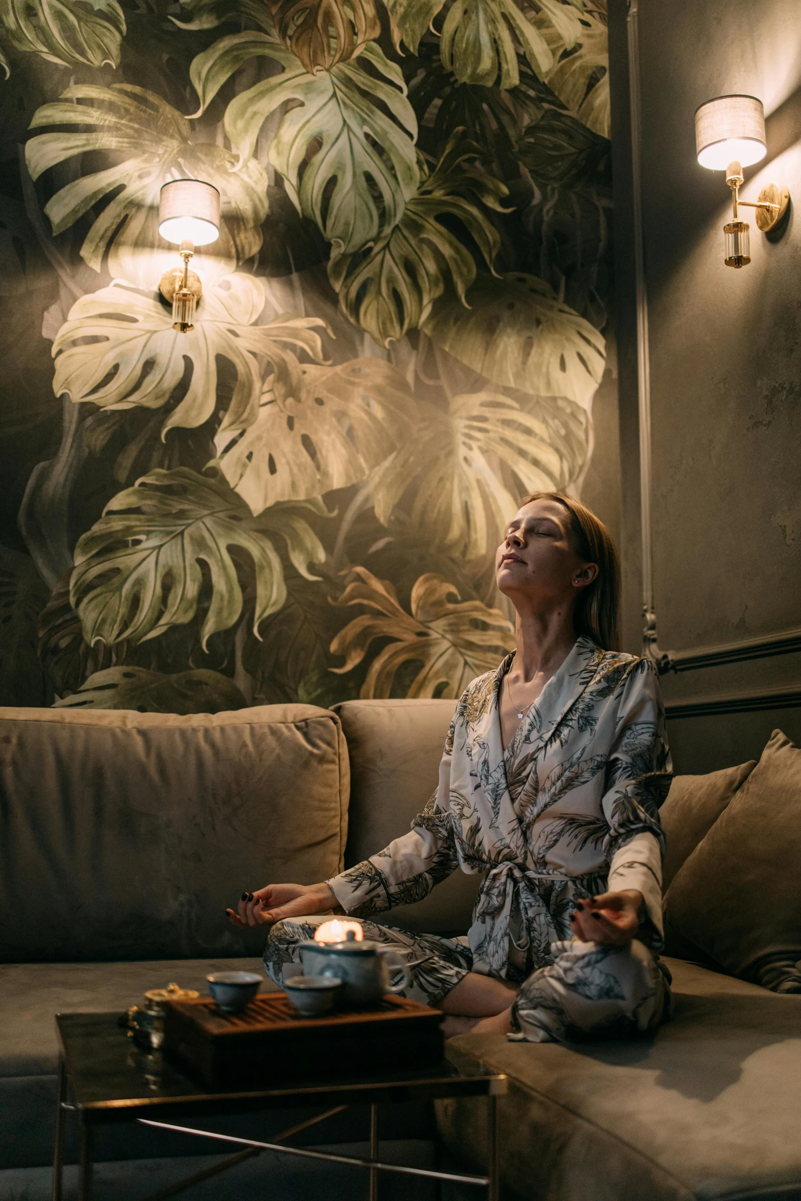 a woman sitting on a couch in a living room, a portrait, inspired by Elsa Bleda, trending on unsplash, renaissance, tea ceremony scene, wallpaper on the walls, in a silver silk robe, gentleman's club lounge