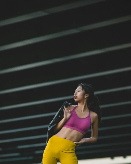 a woman in a pink top and yellow pants, inspired by helen huang, unsplash contest winner, detailed sports bra, asian women, dark backdrop, on rooftop