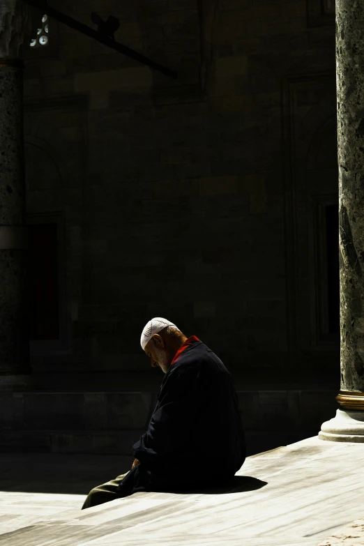 a man sitting on the ground in front of a building, unsplash, renaissance, mourning, peter eisenman, left profile, turkey