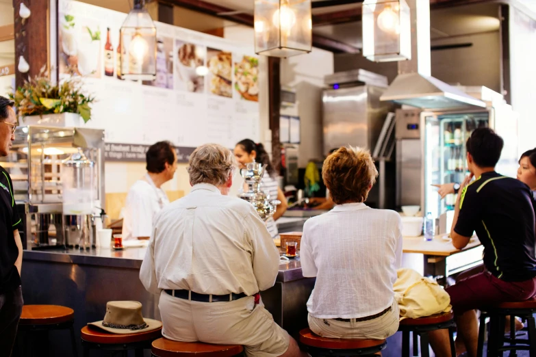 a group of people sitting at a bar, by Elizabeth Durack, unsplash, private press, in a kitchen, food stall, with his back turned, very crisp