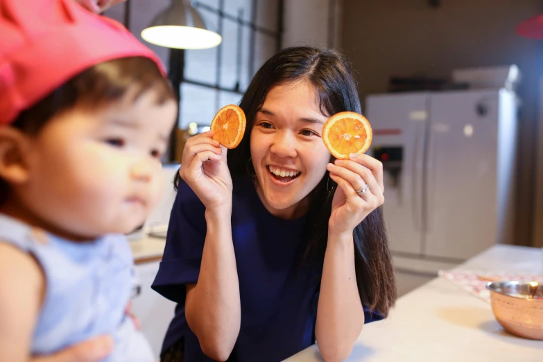 a woman holding two slices of oranges in front of her face, by Juliette Leong, pexels contest winner, children playing with pogs, young cute wan asian face, maternity feeling, behind the scenes photo