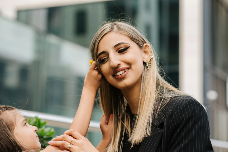 a woman sitting next to a little girl on a bench, an album cover, by Julia Pishtar, trending on pexels, hurufiyya, smiling fashion model face, sitting on a skyscraper rooftop, mia khalifa, close up of a blonde woman