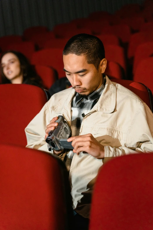 a man sitting in an auditorium looking at his cell phone, a picture, trending on pexels, hyperrealism, imax 7 0 mm. bladerunner, asian male, holding a pair of fans. unreal 5, looking distracted