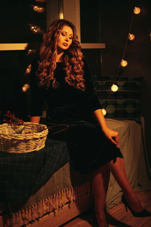 a woman sitting on top of a bed next to a basket, pexels contest winner, renaissance, glowing black dark velvet, retro stylised, christmas night, with long curly hair