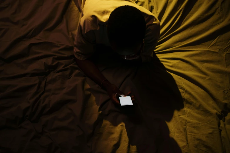 a person laying on a bed with a cell phone, trending on pexels, hurufiyya, standing in a dimly lit room, kano), high angle, hes alone