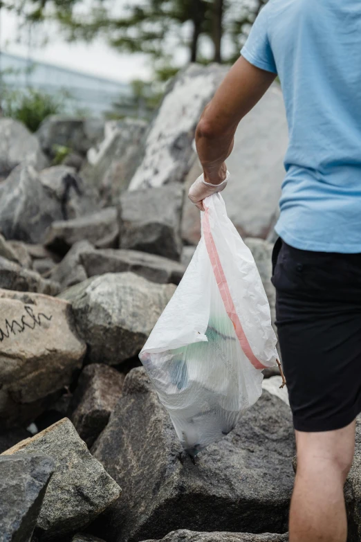 a man holding a plastic bag on top of a pile of rocks, unsplash, harbor, urine collection bag, clean design, woman