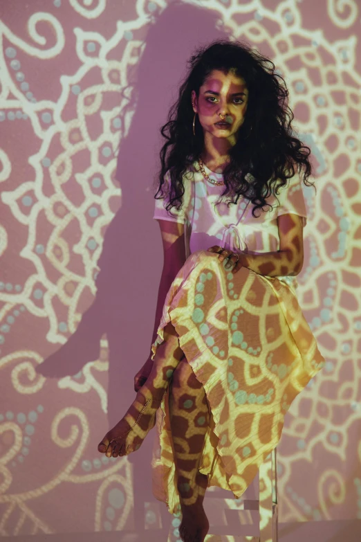 a woman in a yellow dress sitting on a stool, inspired by Barkley Hendricks, trending on pexels, graffiti, with haunted eyes and curly hair, patterned clothing, glowing with colored light, pale light