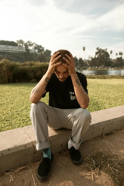 a man sitting on a wall with his head in his hands, a picture, non binary model, trending on r/streetwear, at a park, upset