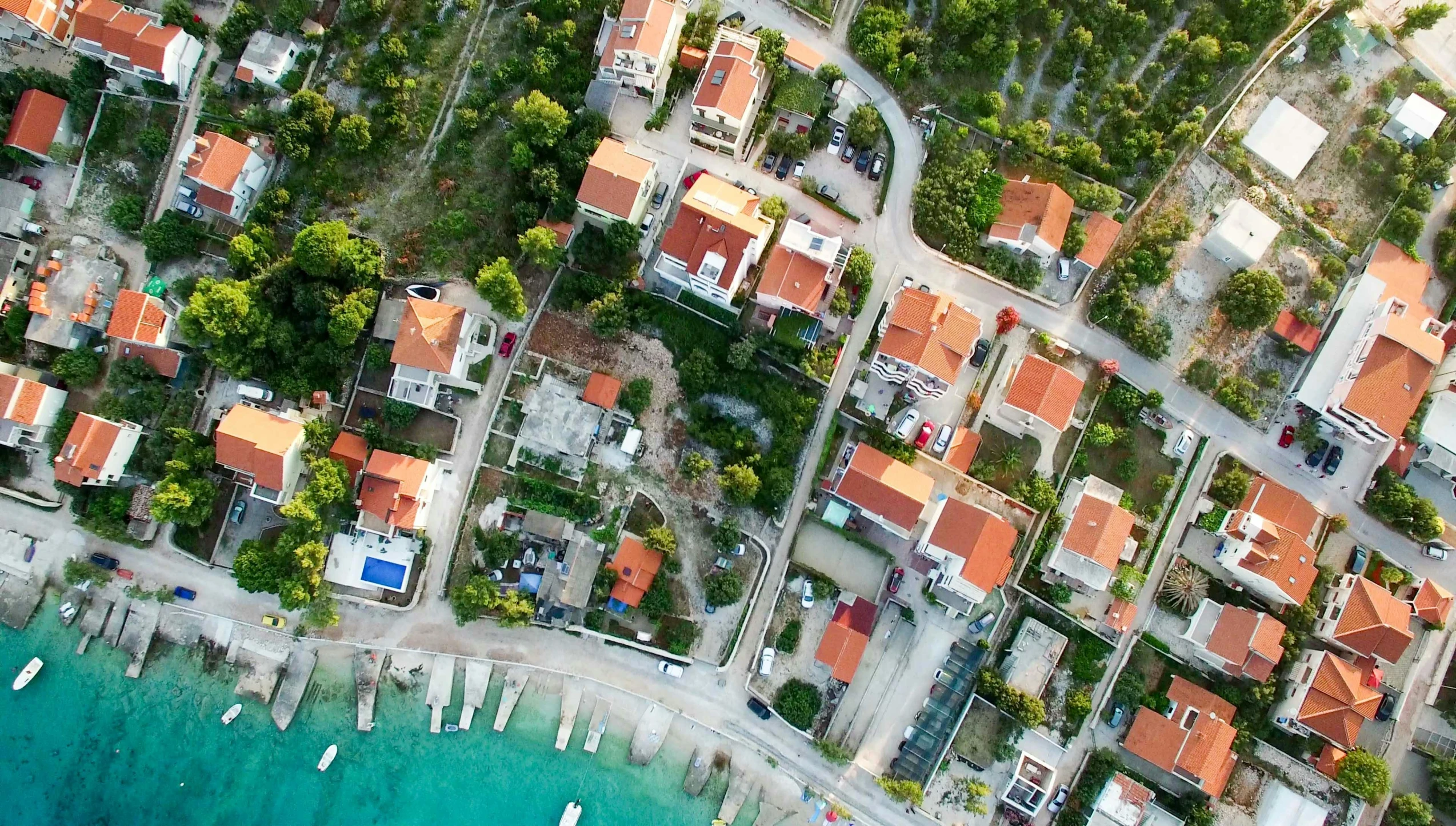 a bird's eye view of a small town next to the ocean, by Emma Andijewska, pexels, orange roof, split near the left, aerial footage, cottages