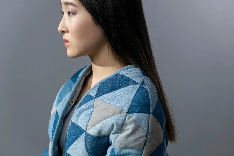 a woman standing in front of a gray background, inspired by Kim Tschang Yeul, wearing blue jacket, quilt, medium close-up, product design shot