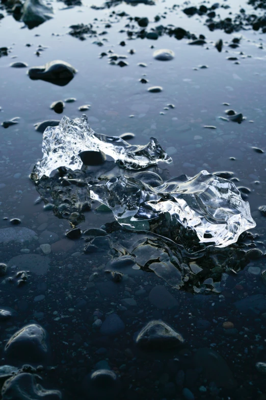 a piece of ice sitting on top of a body of water, unsplash, photorealism, floating rocks, black sand, drops, clear blue water